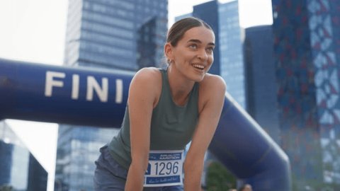 Slow Motion Portrait of a Happy Female City Marathon Runner Crossing the Finish Line and Celebrating her Victory. Female Race Winner Achieving her Goal and Enjoys her Accomplishement Arkistovideo
