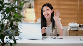 Pretty young asian woman having video call and drinking coffee while sitting in cozy home.