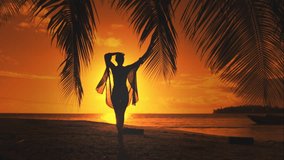 Woman silhouette against orange sunset sky. Young slim woman walking tropical island beach under the coconut palm tree branch. Relaxing, travel, tourism, exotic holiday vacation. Slow motion back view - Powered by Shutterstock - Get 15% off with code: PIKWIZARD15