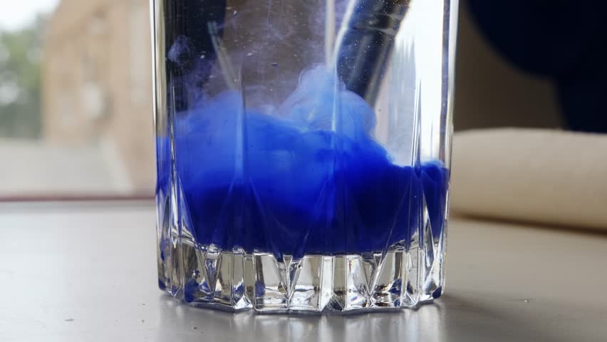 Dissolving blue paint in a glass of water close-up. The artist washes his brush. Ultramarine.
