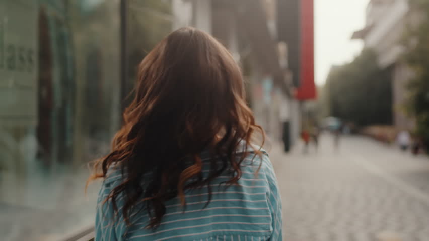 Back view of a charming young asian woman walking down the street and turns around playfully with a smile on her face. Relaxed lady walking on the city centre enjoying beautiful day alone