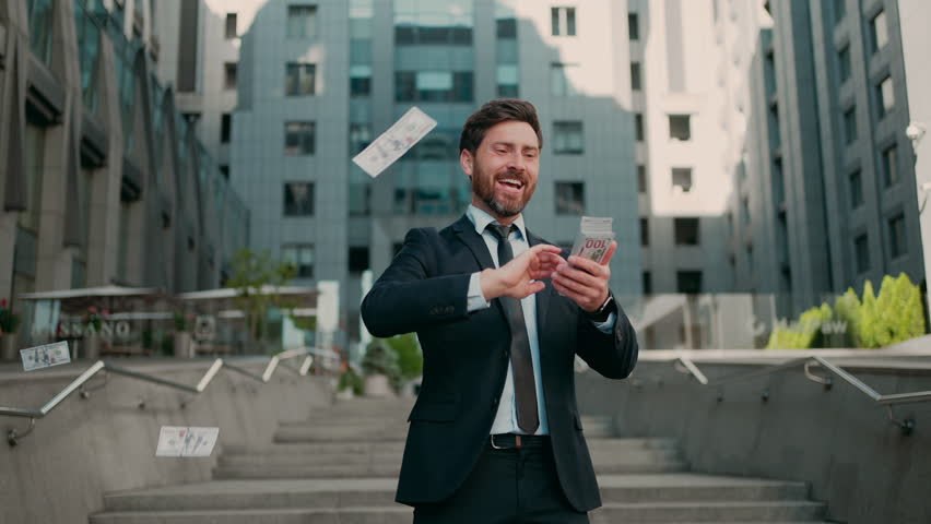 Wealthy man in formal outfit laughs and throws money around standing on stairs in city. Cheerful bearded businessman rejoices receiving large profit slow motion Royalty-Free Stock Footage #1106467743