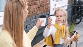 Mother and daughter sit outside and drink hot chocolate. The mother looks at her daughter with love and smiles. Family spending the weekend together. Horizontal video