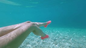 Underwater view of young caucasian woman legs swimming in clear blue turquoise water with fishes in the background. Slow motion under water video of young woman relaxing wearing pink swim shoes