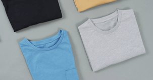 Video of flat lay of t shirts with copy space on grey background. Fashion, trends and clothing concept.