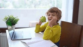 Cute Schoolboy child eating apple while using laptop online educational lesson course at home. Distance learning course remote video conference. Schoolgirl study does school homework.