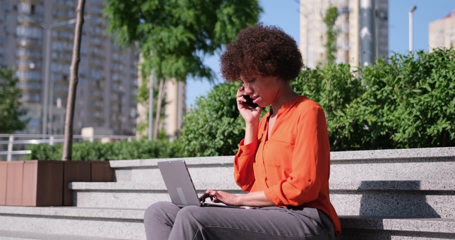 young african american woman sitting on a stairs with laptop online typing working remotely