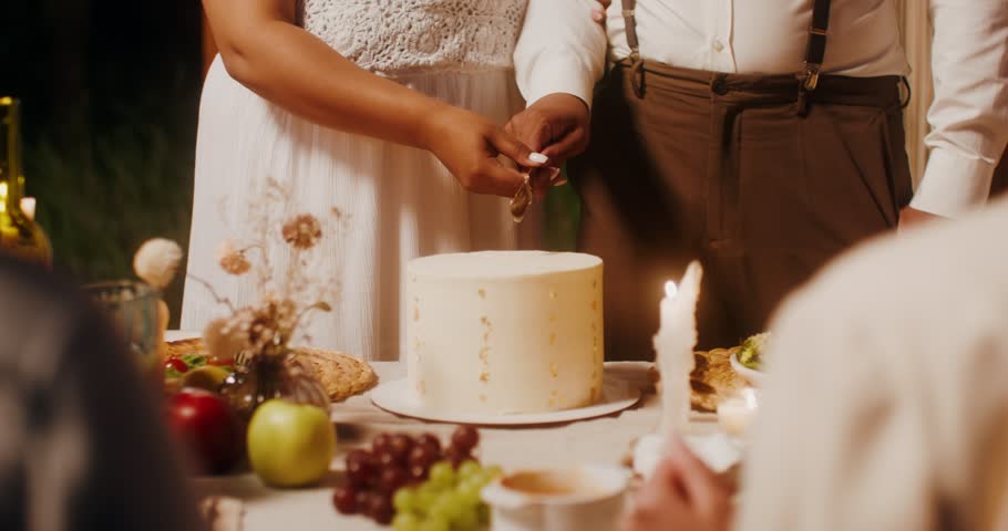 The bride and groom are cutting a wedding cake at an outdoor wedding feast. Close-up of hands, no face Royalty-Free Stock Footage #1106507075