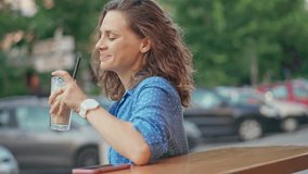 A young cheerful Caucasian woman drinking iced coffee on the outdoor terrace of a cafe on a hot summer day. - Powered by Shutterstock - Get 15% off with code: PIKWIZARD15