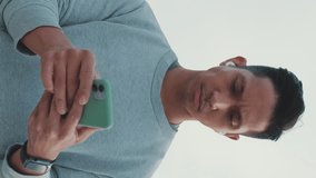 Vertical video, Athlete in wireless headphones, a guy in sportswear, stands on a bridge and uses a mobile phone, listens to music