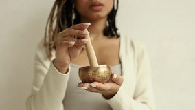 Closeup of young African American female using singing bowl on white background.