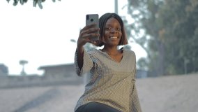 4K video of a young African girl influencer live on her smartphone in an urban park in the middle of the day to create content for her networks or on a video call. 