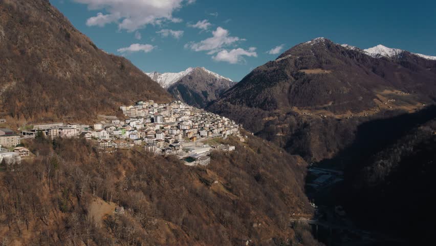 Aerial view of the small village of Premana in Valsassina with the snow-capped mountains of the Lombardy Alps in the background. Blue sky, suggestive panorama. 