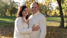 Husband and wife in white warm clothes posing for the camera in the autumn park on a sunny day. Horizontal video