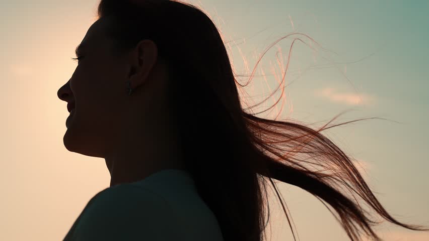 Girl hair flutters in wind, they believe in goodness, women dream of love. Portrait of girl, sun day, silhouette. Beautiful flowing female brown hair. Young woman looks at sky, prays, religious man.