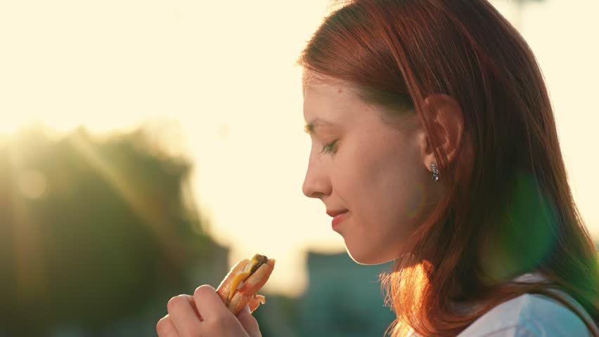 Hungry girl eat burger from fast food on walk. Young woman having snack outdoor. Concept fast food. Enjoy delicious food. Girl eat in Street. Snack in fresh food. People satisfy hunger. Teenager foods Royalty-Free Stock Footage #1106528475