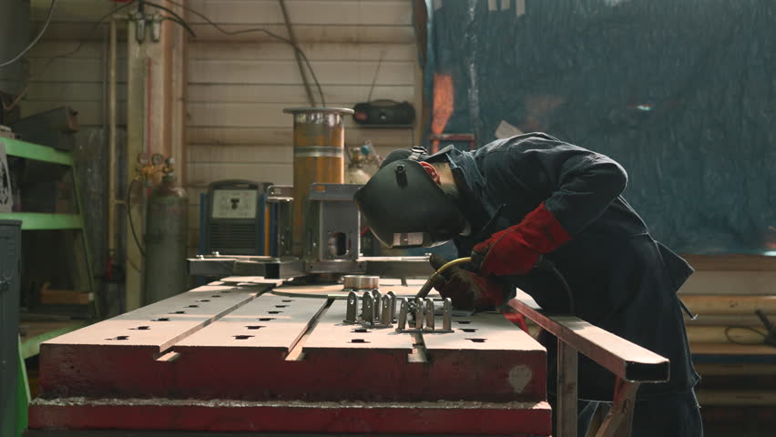 Professional heavy industry worker welder in protective mask and suit works with metal construction on factory. Creative. Steel and iron welding construction site, welding machine with sparks and Royalty-Free Stock Footage #1106529883