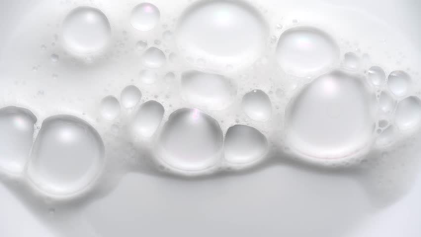 Foam bubbles background. Moving Soap foam popping bubble, white backdrop. Soap sud macro structure. Soap foam close-up. Clean, cleaning concept, laundry, shower. Slow motion