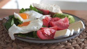 Unrecognizable woman eating meal, plate with arugula, tomatoes, camembert brie cheese, avocado and fried eggs. High quality 4k footage