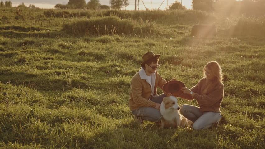 Young married couple taking border collie dog with them for walk or date. Guys fooling around and having fun with pet, wearing brown cap or hat on head. Lifestyle and spending time together concept.