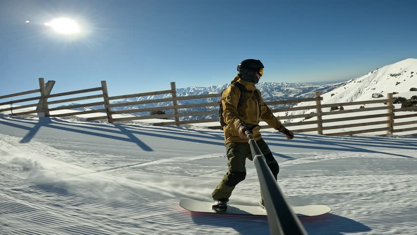 Male millennial cheerful snowboarder having fun snowboarding backcountry on sunny winter day in snowy mountains. Extreme freeride snowboarders riding on snowy track and doing powder turns off piste
