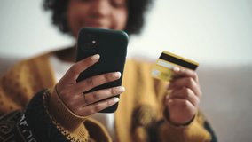 Positive african american woman doing online payment on smartphone using credit card in marketplace. Girl buys in internet at home. Online shopping, customer. Enters bank card number in online store. - Powered by Shutterstock - Get 15% off with code: PIKWIZARD15