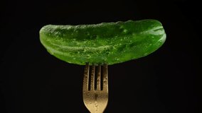Fresh green cucumber on fork, isolated on black background