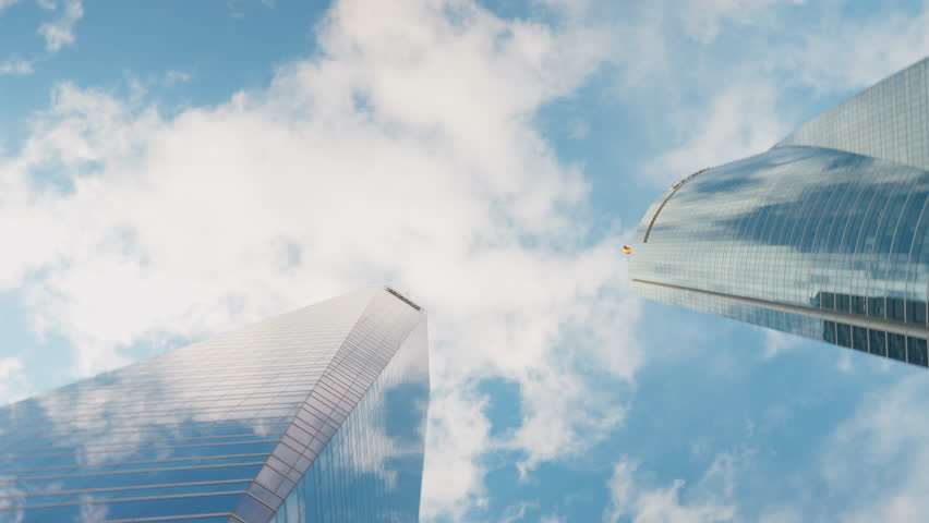 Bottom angle view urban skyscrapers with live camera spinning. Huge glass business buildings at background of blue sky with white clouds outdoors