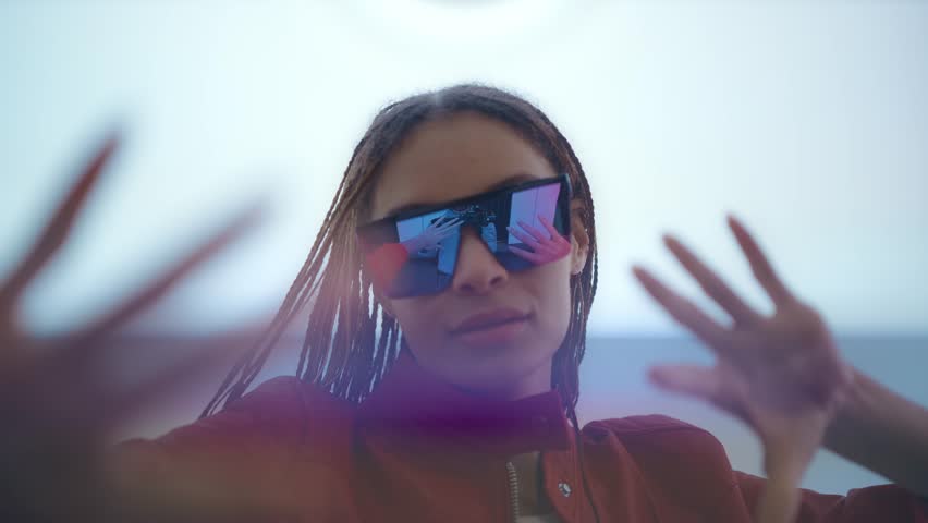 Alternative young woman with futuristic look and fashionable clothes in a bright led screens illuminated tunnel