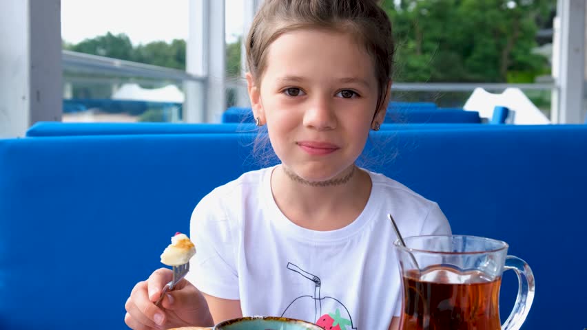 A young girl has breakfast with cheesecakes in a summer cafe.