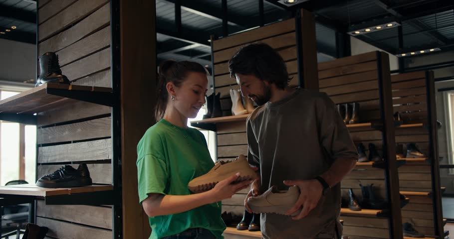 A customer, a man in a brown T-shirt, and a woman employee in a shoe store in a Green T-shirt are talking about choosing shoes Royalty-Free Stock Footage #1106555311