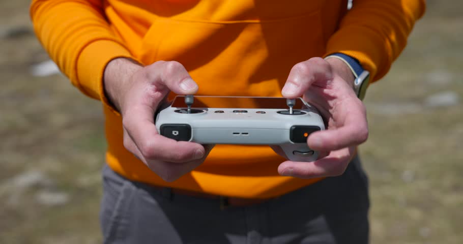 Drone pilot wearing orange jacket using controller of Dji Drone, high angle