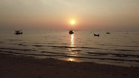 Static shot from beach showing stunning sunset in Thailand with local fishing boat silhouettes.