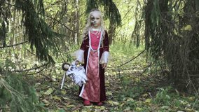 Girl child posing in the forest in a medieval dress in the image of a dead princess. Girl holding a doll. Horizontal video