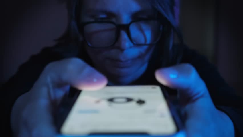 In blue neon light nervous smiling adult woman virtual networks flipping social media feeds watching videos late at night. Female portrait of a young girl student holding a smartphone close up | Shutterstock HD Video #1106567433