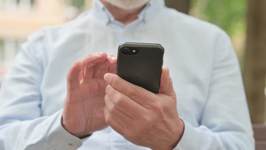 Close Up of Senior Old Man Browsing Smartphone while Sitting Outdoor on a Bench