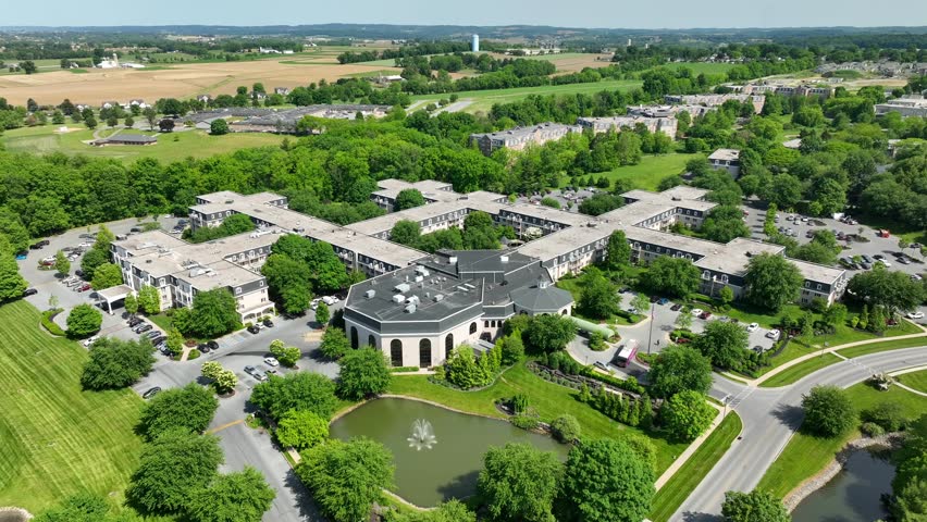 Panoramic view of an expansive apartment complex community surrounded by beautiful landscaping next to a small lake with a fountain.