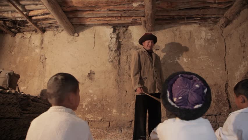 1930s Kyrgyzstan. The first school in the villages. Children study in a dilapidated hut and sit on straw. The teacher stands and explains