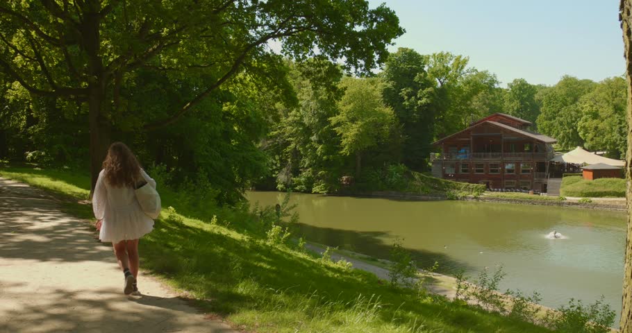 Beautiful woman in a white dress walking next to the Robinson restaurane chalet in Bois de la Cambre in Brussels, Belgium