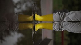 A young woman in yellow rubber boots jumps on a puddle in autumn weather. Girl in yellow rubber boots jumping into a puddle. Carefree young woman in new yellow rubber boots jumps into a big puddle.