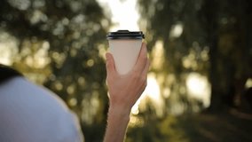 paper cup with coffee in a male hand on a natural background, close-up. A man's hand holds a white paper coffee cup with a black lid. Man holding eco zero waste white paper cup copy-space mockup