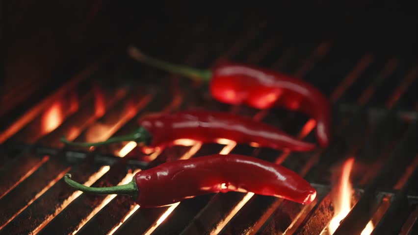 Red Pepper on the Grill With Fire. Vegetables on grill barbecue outdoors. Cooking roasted hot chilli peppers on barbecue gas grill. BBQ on Black Background, outdoors
