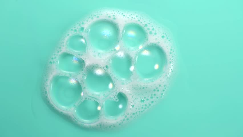 Foam bubbles popping over turquoise background, close up. Soap bubble, Soap sud macro structure. Clean, cleaning concept, laundry, shower gel