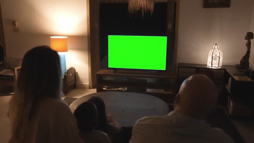 Happy Family of Parents with Young Kids Watching TV and Sitting on Sofa. People Inside at Home Watch News on Television Display Mockup. Children on Couch Looking at White Screen of Chroma Key Mock-Up