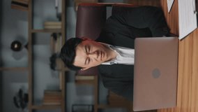 Vertical video of anxious asian manager putting hands on his head after watching clip on laptop in office. Shocked business leader discovering stunning information about recent events online.