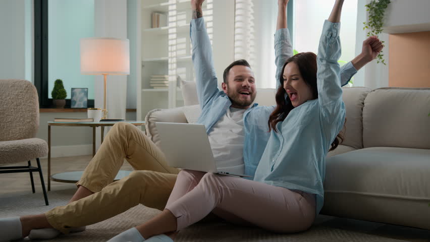 Excited happy young family win with laptop at home floor achievement online victory couple man woman husband wife winning with computer internet achieve kissing celebrating applauding betting success | Shutterstock HD Video #1106596741