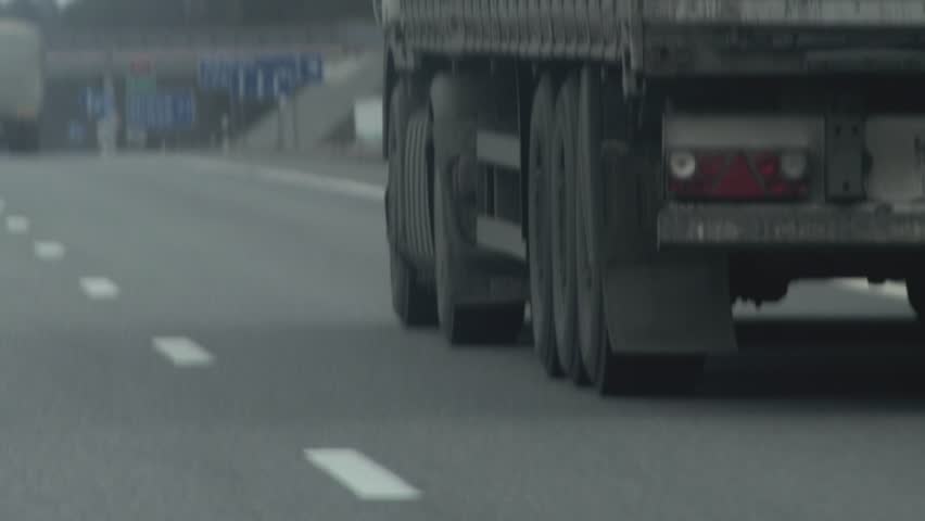 Trucks with a semi-trailer drive along the highway in gray cloudy weather in motion. Lots of wheels, axle load. overload. Slow motion