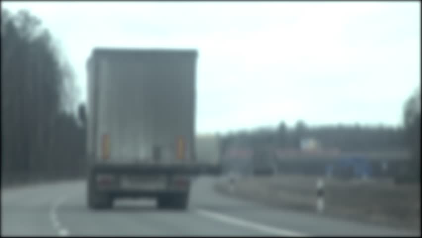 Trucks with a semi-trailer drive along the highway in gray cloudy weather. Blurred, copy space for text. Slow mo