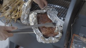 This video shows delicious pork belly meat being taken out of a smoker grill with tongs.