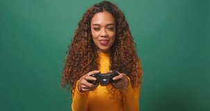 Young biracial woman plays game with console girl gamer, green studio background